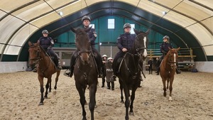 Policjanci na koniach podczas egzaminu, w tle policjanci z tarczami i pałkami
