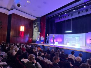 Policjant w towarzystwie dwóch kobiet stoi na scenie i mówi do mikrofonu