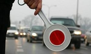 Ręka policjanta, który stoi przy drodze i trzyma tarczę do zatrzymywania pojazdów