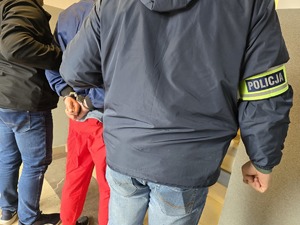 Nieumundurowani policjanci doprowadzają zatrzymanego w kajdankach