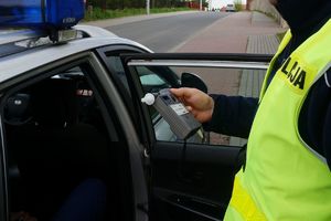 Policjant przy radiowozie trzyma urządzenie do badania stanu trezźwości
