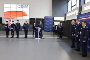 Policjanci stoją w auli a dwóch mężczyzn stoi przy mównicy
