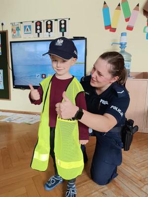 Policjantka pozuje do zdjęcia z chłopcem w policyjnej czapce i kamizelce z napisem policja
