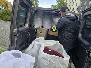 Policjant stoi przy samochodzie w którym znajdują się zabezpieczone worki z odzieżą