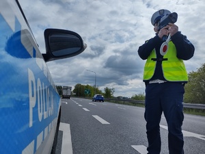 Policjantka mierzy prędkość na drodze stojąc przy policyjnym radiowozie