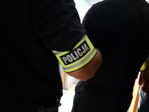 Opaska policyjna na przedramieniu policjanta, który doprowadza zatrzymanego