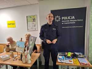 Policjant przy stoisku na którym znajdują się książeczki i ulotki na temat bezpieczeństwa
