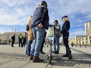 Mężczyzna z hulajnogą podczas rozmowy z dziennikarzami, w tle policyjny patrol