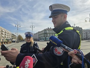 Policjant trzyma urządzenie w ręce, wokół niego mikrofony dziennikarzy