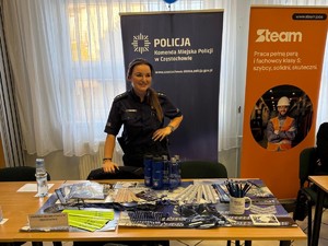 Policjantka na stanowisku prewencyjnym prezentuje ulotki i gadżety