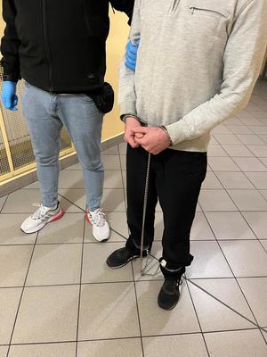 Zatrzymany w kajdankach zespolonych trzymany pod rękę przez nieumundurowanego policjanta