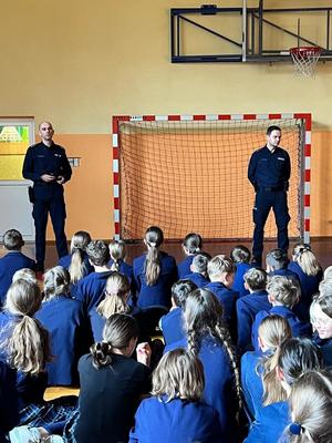 Policjanci podczas prelekcji rozmawiają z dziećmi w sali gimnastycznej