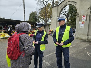 Policjanci pod cmentarzem wręczają kobiecie odblask