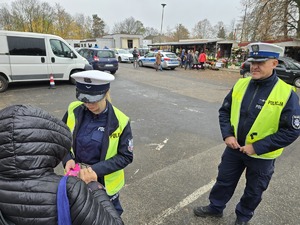 Policjanci wręczają odblask kobiecie, która znajduje się przed cmentarzem