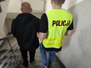 Policjant doprowadza zatrzymanego mężczyznę po schodach
