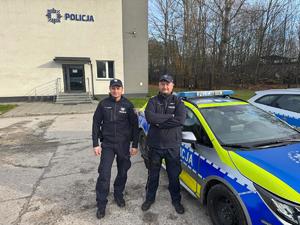 Dzielnicowi w umundurowaniu służbowym stoją przed komisariatem przy radiowozie