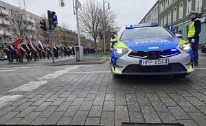 Policyjny radiowóz a przy nim policjanci, którzy zabezpieczają przemarsz
