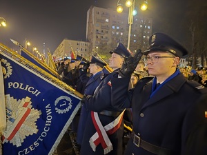 Policjanci stoją ze sztandarem i oddają honor
