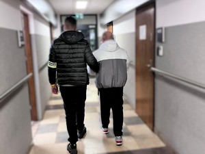 Nieumundurowany policjant doprowadza korytarzem zatrzymanego
