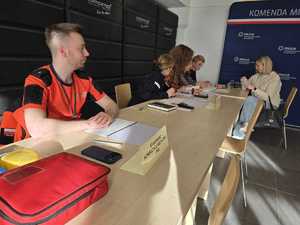 Osoby rekrutujące uczestników siedzą przy stoliku z dokumentami