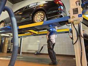 Pojazd w warsztacie samochodowym na podnośniku, pod nim mechanik samochodowy dokonuje kontroli stanu technicznego