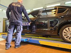 Policjant zamieszcza naklejkę z napisem Policja na karoserii pojazdu