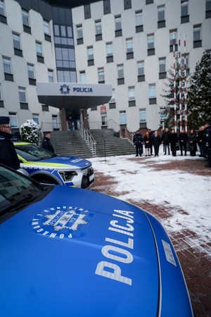 Element policyjnego radiowozu- pokrywa silnika z napisem Policja- pomagamy i chronimy na tle budynku komendy