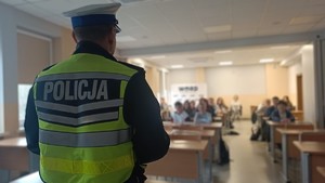 Policjant w sali rozmawia z uczniami w ławce