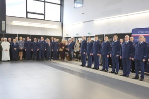 Zgromadzeni uczestnicy stoją w auli wśród policjantów