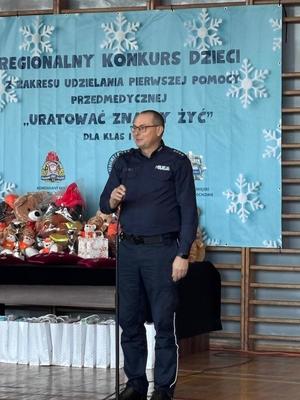 Policjant przemawia do mikrofonu w sali gimnastycznej gdzie odbywa się konkurs