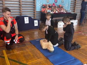 Uczniowie udzielają pierwszej pomocy poszkodowanemu, ich zadaniu przygląda się ratownik medyczny