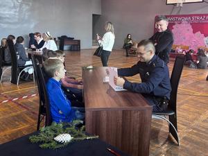 Policjant przy stoliku rozmawia z uczniami podczas konkurencji