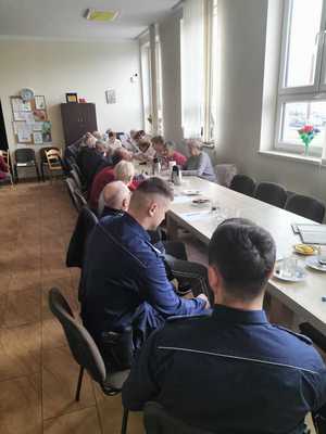 Policjanci razem z seniorami siedzą przy stole i rozmawiają