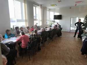 Policjant prowadzi debatę z seniorami, którzy siedzą przy stoliku