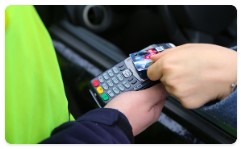Zdjęcie poglądowe- ręka policjanta trzyma terminal płatniczy przy samochodowym oknie kierującego pojazdem