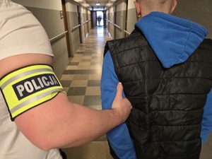 Nieumundurowany policjant trzyma pod rękę zatrzymanego męzczyznę