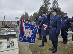 Policjanci ze sztandarem policyjnym oddają honor na cmentarzu