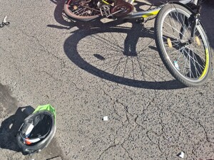 Wywrócony rower na drodze, obol leży kask ochronny