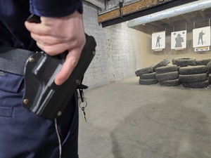 Ręka policjanta trzymana na rękojeści broni, która znajduje się przy pasie w kaburze