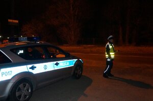 Policjant stoi przy drodze, obok zaparkowany radiowóz