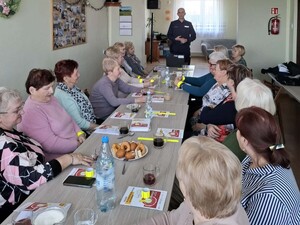 Policjant rozmawia z seniorami, którzy siedzą przy stoliku