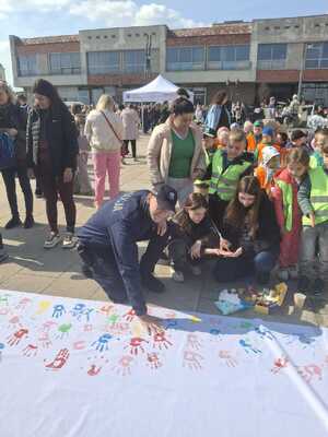 Policjant wśród dzieci odbija swoją pomalowaną dłoń na podłożu