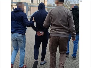 Nieumundurowani policjanci doprowadzają zatrzymanego w kajdankach założonych na ręce trzymane z tyłu