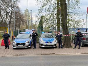 Policjanci przy radiowozach patrolują rejon przy stadionie sportowym
