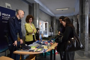 Policjant i kobieta rozmawiają przy stoisku policyjnym z młodzieżą