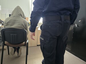Mężczyzna podczas przesłuchania w pomieszczeniu służbowym, obok stoi policjant