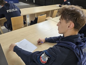 Policjant siedzi przy stoliku na którym leży test z kartą odpowiedzi