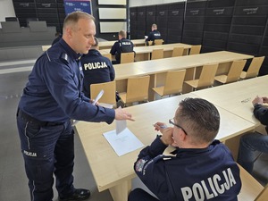 Policjant rozdaje testy policjantom, którzy przystępują do konkursu