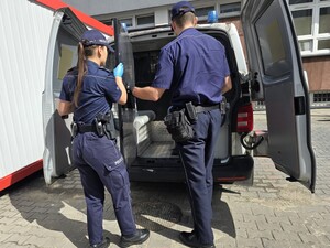 Policjanci otwierają drzwi radiowozu za którymi są kraty