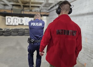 Policyjny instruktor stoi za policjantem, który strzela z broni w kierunku tarczy